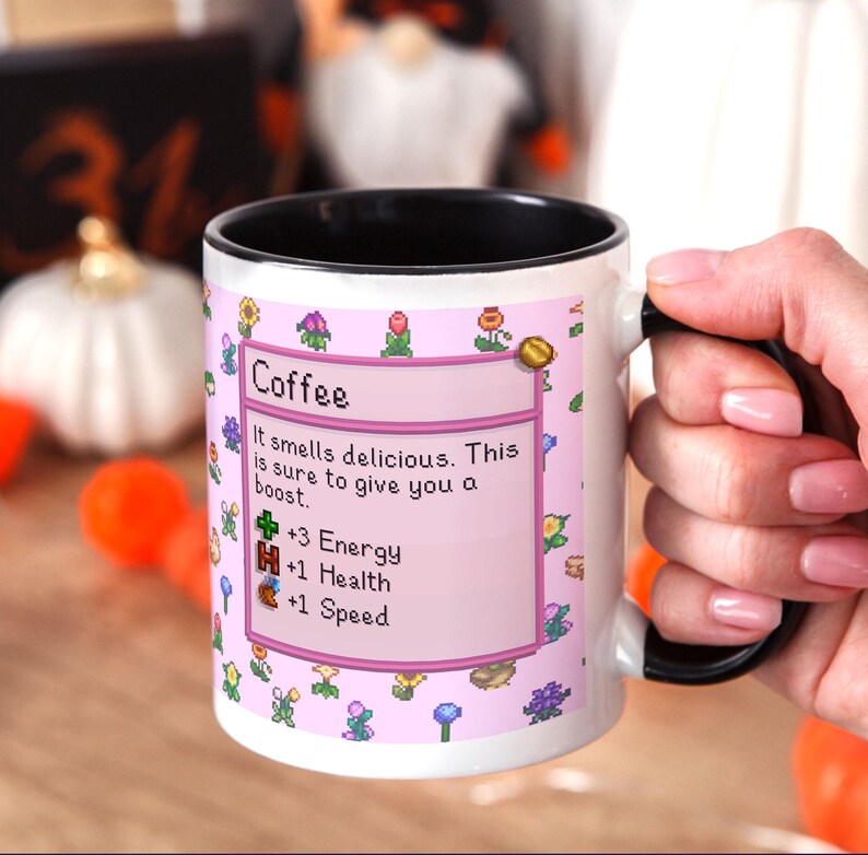 May include: White coffee mug with a black interior and handle. The mug features a pink label with the word "Coffee" and text that reads "It smells delicious. This is sure to give you a boost." with pixelated graphics.