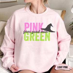 May include: Light pink sweatshirt with the text "PINK goes good with GREEN" in pink and green block letters. A black witch hat graphic is above the word "GREEN". The words "LIGHT PINK" are in a small box at the bottom.