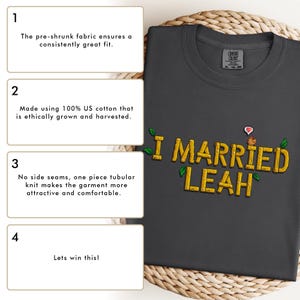 May include: A dark gray t-shirt with the text "I MARRIED LEAH" in a pixelated font. The text is surrounded by green leaves and a small pixelated chicken with a heart above it.
