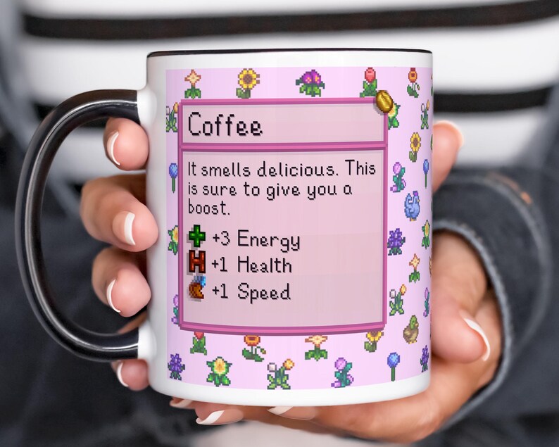 May include: White ceramic coffee mug with a black handle and rim. The mug features a pink background with pixelated flowers and a text box that reads "Coffee". The text box also includes the phrases "It smells delicious. This is sure to give you a boost."