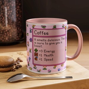 May include: A pink coffee mug with a matching handle and interior. The mug features pixelated floral designs and the word "Coffee" with text that reads "It smells delicious. This is sure to give you a boost. +3 Energy +1 Health +1 Speed."