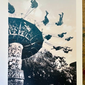 Puede incluir: Una fotografía en blanco y negro de un carrusel vintage con personas montando en los columpios. El carrusel está en un parque con árboles en el fondo.