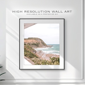 Puede incluir: Una fotografía enmarcada de un paisaje costero con un acantilado rocoso y olas del océano rompiendo en la costa. La foto está en un marco negro y está colgada en una pared blanca.