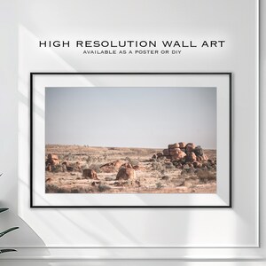 May include: A framed photograph of a desert landscape with large, rounded rocks in the distance. The sky is a pale blue and the ground is a light brown.