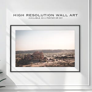 May include: A framed photograph of a large rock formation in a desert landscape. The rock is a light brown color and is surrounded by dry, brown grass. The sky is a light blue color and there are clouds in the distance.