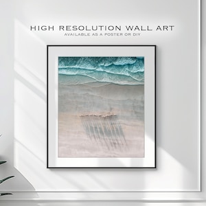 May include: An aerial photograph of a sandy beach with turquoise ocean waves breaking on the shore. The shadows of a group of people walking along the beach are visible in the sand.