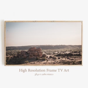 May include: A framed photograph of a rocky landscape with a clear blue sky. The rocks are a reddish-brown color and are scattered across the landscape. The sky is a light blue with a few clouds. The photo is framed in a light brown wood frame.