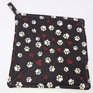 May include: Black quilted pot holder with a white paw print and red heart pattern.