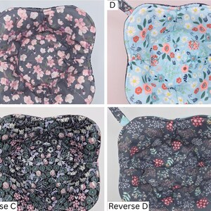 May include: Four quilted bowl cozies with floral patterns. One has a gray background with pink flowers, another has a light blue background with red and orange flowers, and the other two have dark backgrounds with floral designs. Each cozy has a loop for hanging.
