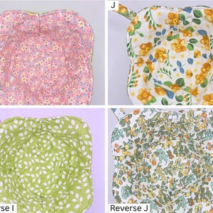 May include: Four fabric bowl cozies with floral patterns. The cozies have a square shape with a handle and are reversible. The patterns include pink, yellow, green, and a mix of floral designs. The cozies are designed to hold bowls.