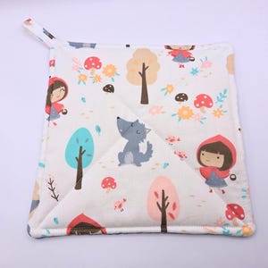May include: A white quilted pot holder with a red hooded girl, a wolf, and trees on a white background. The pot holder has a loop for hanging.