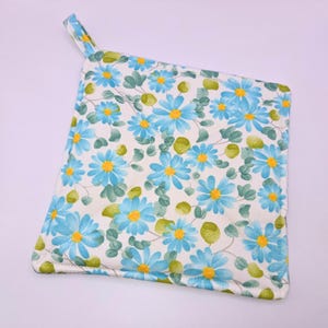 May include: A blue and white floral pot holder with a loop handle. The pot holder is made of fabric and has a quilted design.