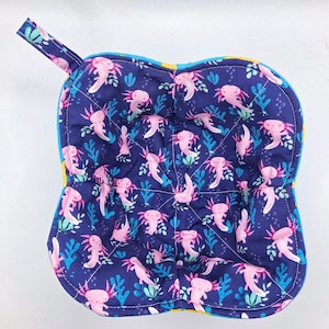 May include: A navy blue, square-shaped pot holder with a loop for hanging. The pot holder features a repeating pattern of pink axolotls and blue seaweed on a navy background. The edges are trimmed with yellow and blue fabric.