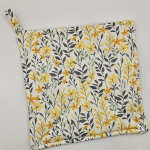 May include: A white pot holder with a yellow floral pattern. The pattern features small yellow flowers and gray leaves on a white background.