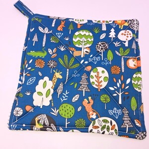 May include: Square blue potholder with a loop for hanging. The fabric features a whimsical forest scene with trees, animals like a giraffe, monkey, and lion, and various floral elements. White stitching outlines the design.