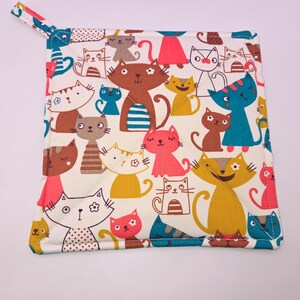May include: A white cotton pot holder with a colorful pattern of cartoon cats. The cats are in various poses and colors, including pink, brown, blue, and yellow.