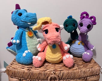 Puede incluir: Cuatro juguetes de peluche de dragón tejidos a mano en varios colores. Uno es azul con espina dorsal morada, uno es color melocotón con detalles amarillos, uno es verde oscuro y uno es morado con vientre azul claro. Tienen ojos oscuros.