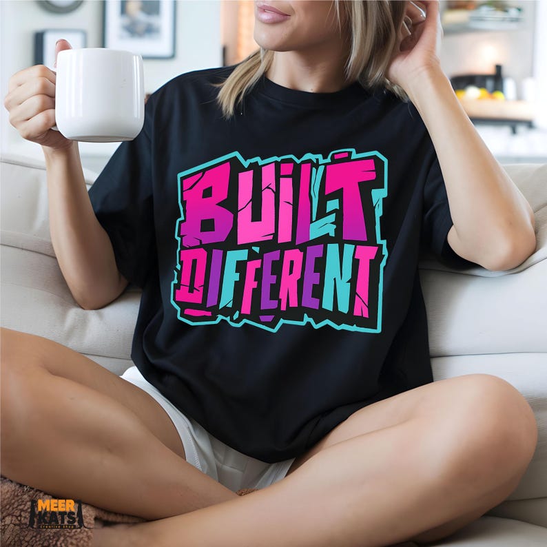 May include: Black t-shirt with the text "BUILT DIFFERENT" in a vibrant, graffiti-style design. The text features a gradient of pink, purple, and blue colors. The shirt is a casual wear item.