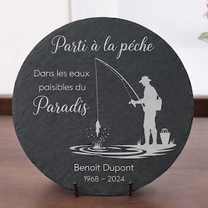 May include: A round, dark gray slate stone with white etched text and a fisherman silhouette. The text reads "Parti &agrave; la p&ecirc;che", "Dans les eaux paisibles du Paradis", and the name "Benoit Dupont" with dates 1968-2024.
