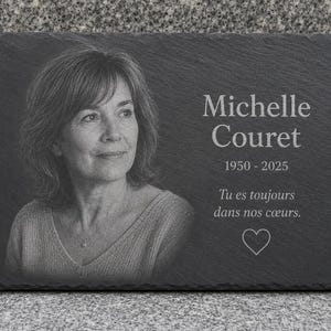 Puede incluir: Una placa conmemorativa rectangular de pizarra gris oscuro con un retrato grabado con láser de una mujer. El texto dice Michelle Couret, 1950-2025, y Tu es toujours dans nos cœurs, acompañado de un pequeño icono de corazón grabado en la piedra.