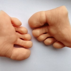 May include: Two realistic-looking, flesh-colored silicone feet with five toes each. The feet are posed as if they are standing on a flat surface.