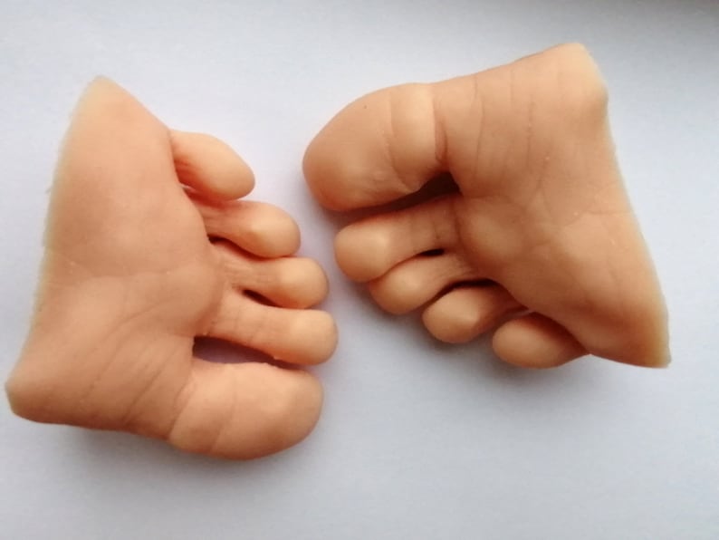 May include: Two realistic-looking, flesh-colored silicone feet with five toes each. The feet are posed as if they are standing on a flat surface.