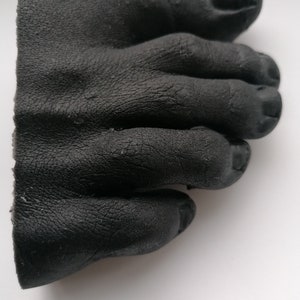 May include: A black rubber foot mold with five toes. The toes are curled and the mold is detailed with wrinkles and creases.
