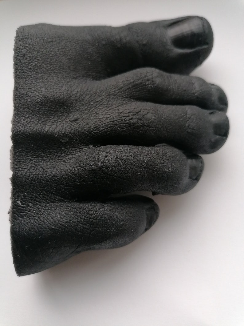 May include: A black rubber foot mold with five toes. The toes are curled and the mold is detailed with wrinkles and creases.