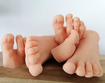 May include: Four realistic-looking silicone baby feet, in various poses, on a wooden surface.