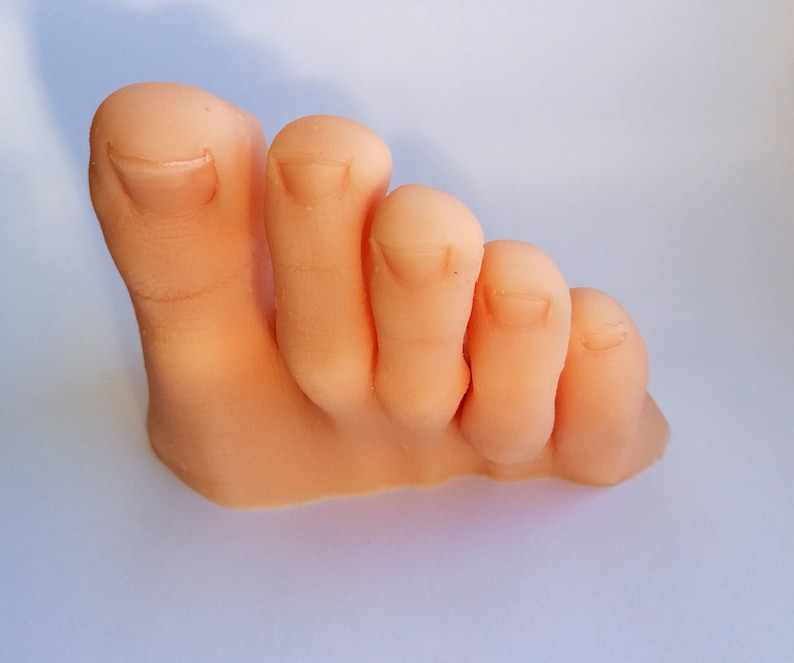 May include: A close-up of a light pink, fleshy, realistic-looking foot with five toes. The toes are slightly curled and the foot is positioned as if it is standing on its side.