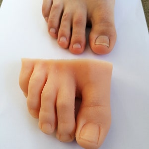May include: A close-up of a pair of realistic-looking silicone feet. The feet are nude in color and have detailed toes and nails.