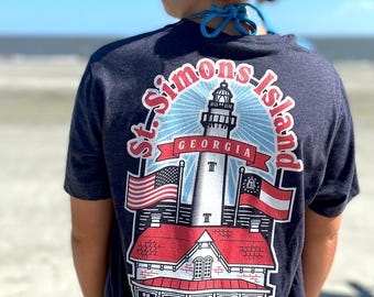 May include: Navy blue t-shirt featuring a graphic of the St. Simons Island lighthouse in Georgia. The design includes the American and Georgia state flags, and the text "St. Simons Island Georgia".
