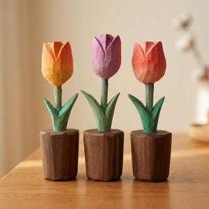 Może przedstawiać: Trzy drewniane rzeźby tulipanów w kolorach pomarańczowym, fioletowym i czerwonym. Każdy tulipan ma zielone liście i brązową doniczkę. Tulipany są wyrzeźbione z widocznym usłojeniem drewna, dodając tekstury.