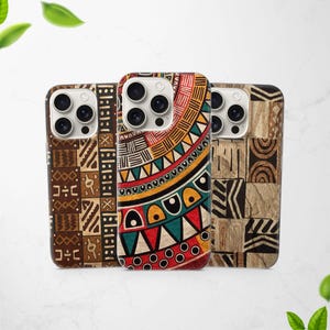 May include: Three mobile phone cases with vibrant, geometric tribal patterns. The cases showcase diverse designs in shades of brown, red, yellow, and green. The cases are presented on a white surface with green leaves in the background.