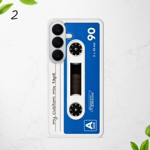 Puede incluir: Una funda de smartphone blanca con un gr&aacute;fico de casete azul. El dise&ntilde;o incluye el texto "my custom mix tape", "90", "2 x 45 min", "Compact Cassette" y "A SIDE". La funda tiene tres aberturas circulares para las lentes de la c&aacute;mara.