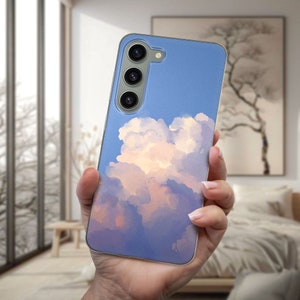 Könnte beinhalten: Eine transparente Handyhülle mit einem Aquarellbild einer flauschigen weißen Wolke vor blauem Himmel. Die Hülle hat einen Ausschnitt für eine Dreifach-Kamera.