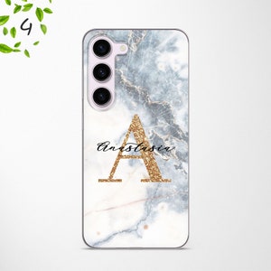 May include: A white phone case with a marble pattern and a gold glitter letter A with the name Anastasia written in cursive below it.