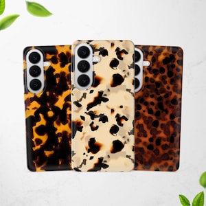 May include: Three phone cases with a tortoiseshell pattern. The cases feature a camera cutout and a glossy finish. The patterns vary in color, with shades of brown, black, and cream. The cases are designed to protect the phone.