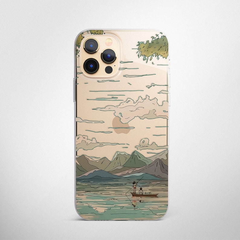 May include: A clear phone case with a Japanese-inspired design featuring a mountain landscape, a lake, and two people in a boat. The case has a gold background with a light blue and green design.