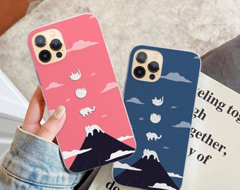 May include: Two phone cases featuring a mountain and white cats design. The case on the left is pink with white clouds and the case on the right is blue with white clouds.