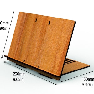 May include: A wooden book stand with a natural wood grain finish. The stand is 9.05 inches wide, 5.90 inches deep, and 5.90 inches tall. It features a sloped design for holding books and a small ledge to keep pages in place.