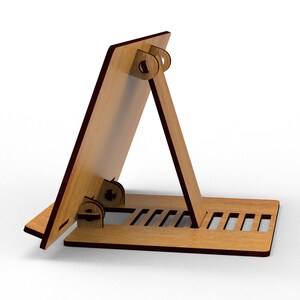 May include: A wooden tablet stand with a light brown finish and dark brown edges. The stand is designed with a base, an angled support, and a back panel, all connected with interlocking joints. The base features several rectangular cutouts.