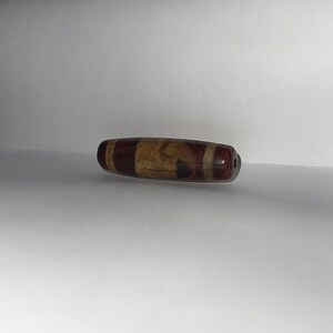 May include: A brown and white striped cylindrical bead with a hole through the center.