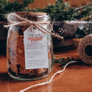 Könnte beinhalten: Ein Glasgefäß gefüllt mit Orangenscheiben, Zimtstangen und anderen Gewürzen. Ein am Glas befestigtes Etikett lautet "Let's make magic" und enthält Anweisungen zum Herstellen einer Sauce.