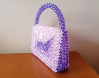 May include: A small, beaded handbag with a purple handle and a pink and purple ombre design.