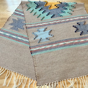 May include: Two woven table runners with fringe edges. The runners feature a geometric pattern with blue, red, green, and yellow accents.