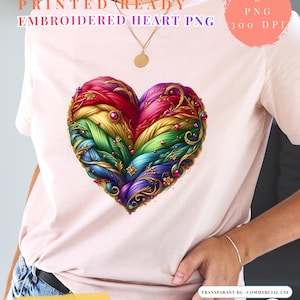 Puede incluir: Una camiseta rosa claro con un gran diseño de corazón bordado. El corazón es una vibrante mezcla de colores del arcoíris, con detalles y adornos intrincados. El texto en la camiseta dice "PRINTED READY EMBROIDERED HEART PNG".