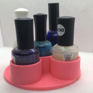 May include: A pink, circular nail polish organizer holding several bottles of nail polish. The bottles are various colors, including purple, blue, and iridescent. The organizer has several circular compartments to hold the bottles upright.