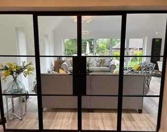 May include: A black metal framed glass door with multiple panes, revealing a living room with a black and white patterned sofa, a white sofa with yellow and black pillows, and a wooden floor.