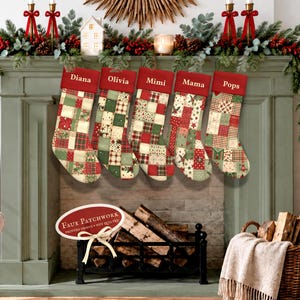Five personalized patchwork style Christmas stockings in traditional red, green and cream hanging from a sage green fireplace mantel with festive holiday greenery.
